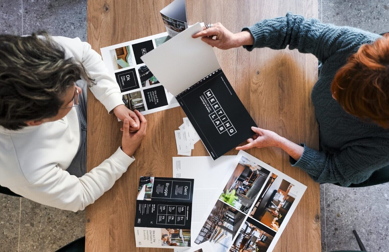 Top view van een man en een vrouw die tegenover elkaar zitten met verschillende papieren op tafel over MeetingLab
