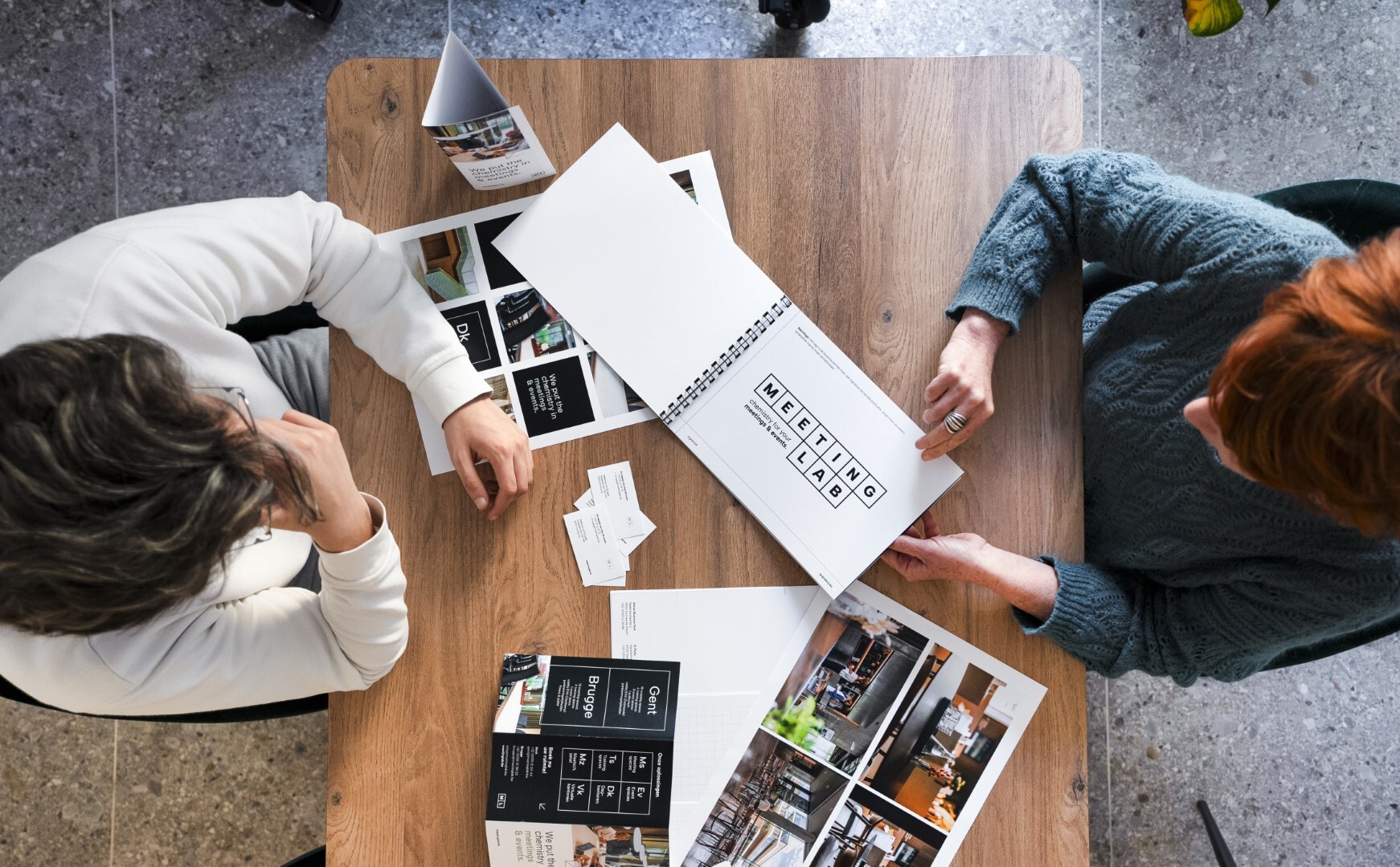 Foto van bovenaf met 2 personen die tegenover elkaar zitten met mock-up brochures voor hun