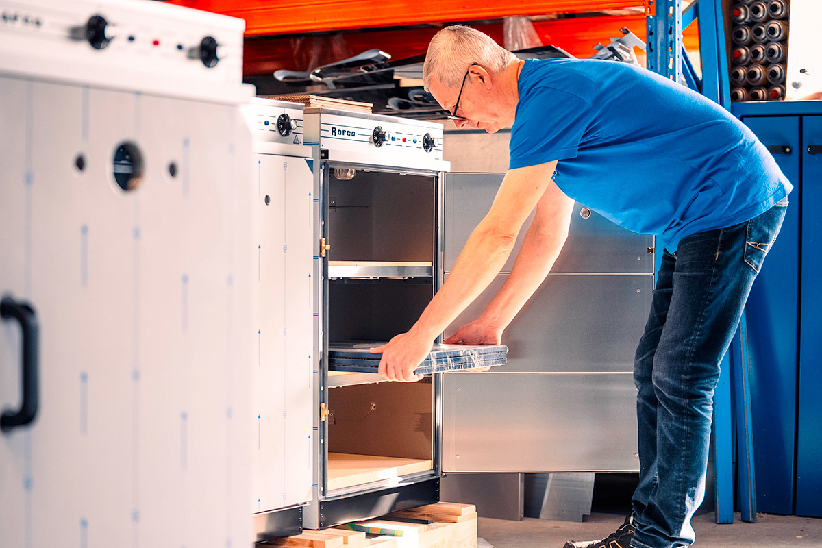 Man in blauw T-shirt plaatst een metalen lade in een industriële oven in een werkplaats.