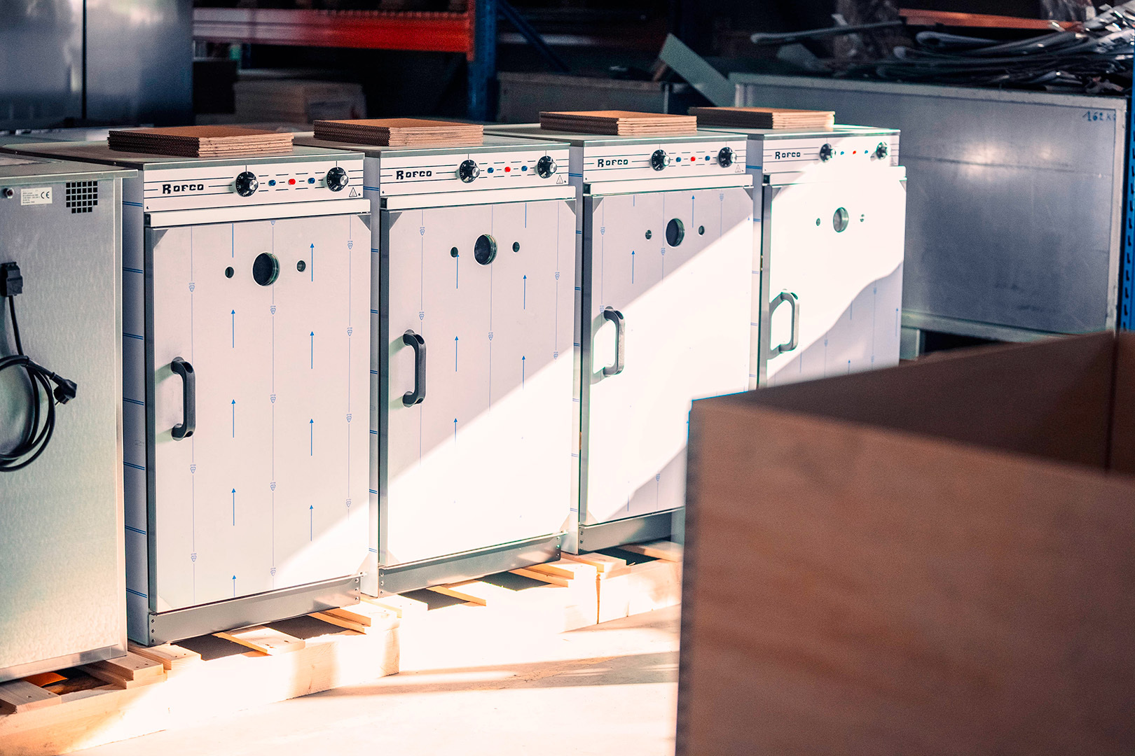 Rij industriële ovens op houten paletten in een magazijnruimte met invallend zonlicht.