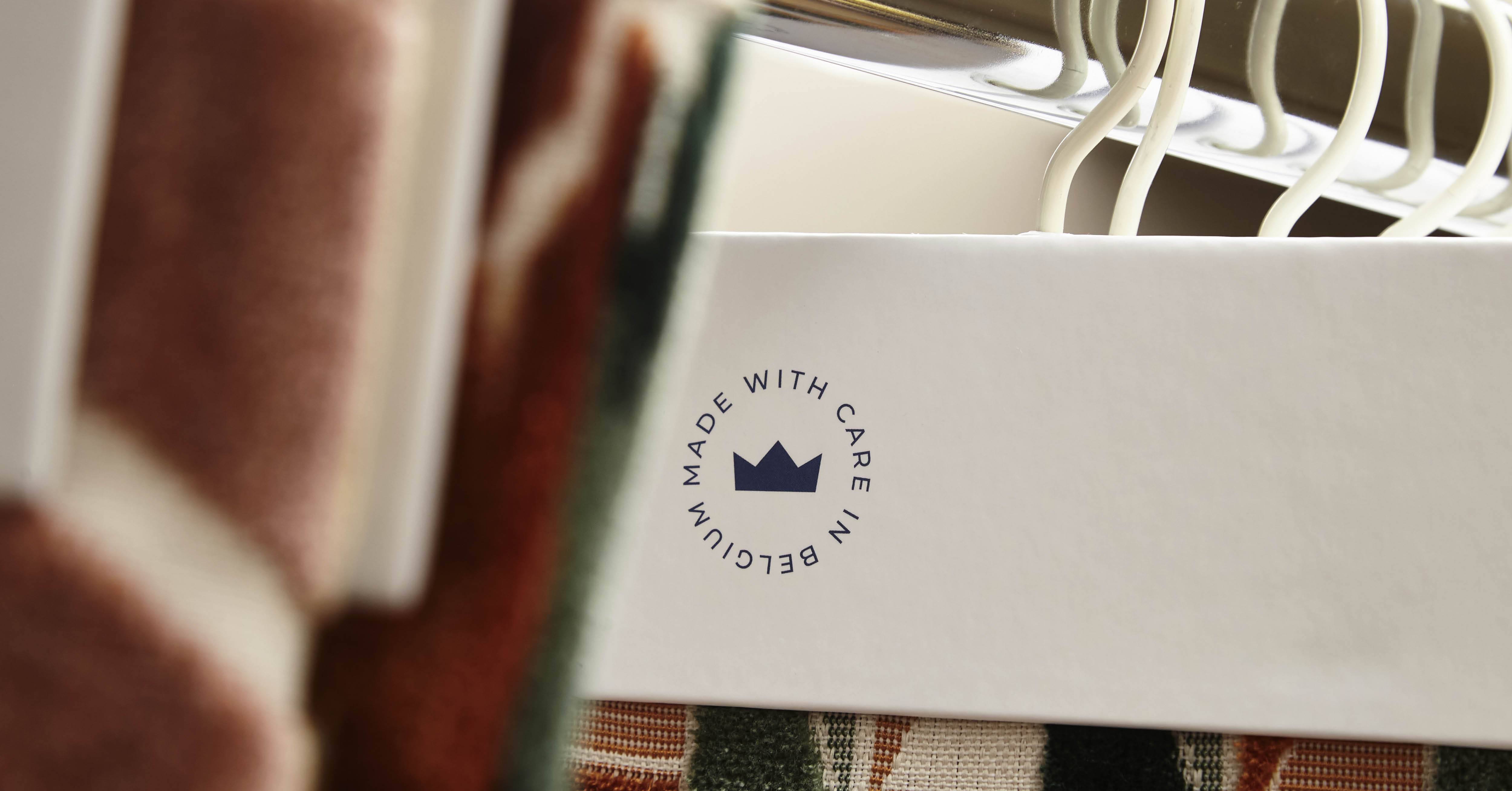 Logo op een plank tussen rek met verschillende stoffen "Made with care in Belgium"
